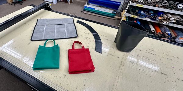 Two small tote bags, one red and one green, on a worktable with fabric and pattern tools.